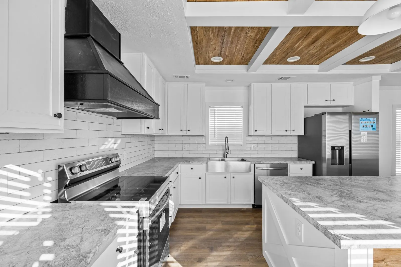 White kitchen with coffered wood ceiling, black range hood and farmhouse sink